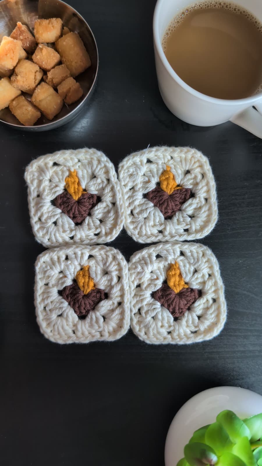 Four finished diya granny squares arranged beside chai, sweets, and a small plant